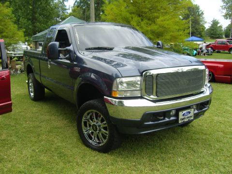 2007 Ford Mustang - A dark blue pickup truck with custom chrome wheels and grille is parked on a grassy field, with other vehicles in the background.