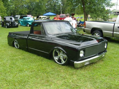 2007 Ford Mustang - A heavily modified black pickup truck sits low on its suspension at a car show, surrounded by other vehicles and attendees.