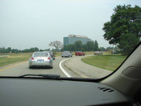 1992 Ford Taurus - A silver Nissan 350Z is seen from behind on a highway, with other vehicles and an office building in the distance.