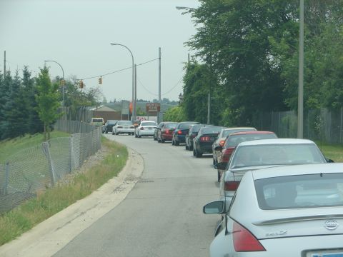 1992 Ford Taurus - A line of vehicles is seen on a road, with trees and a fence bordering the scene.