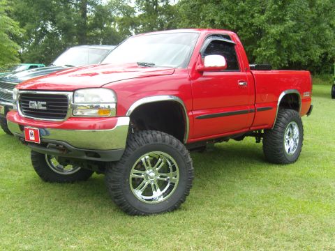 2007 Ford Mustang - Lifted red GMC Sierra pickup truck with chrome wheels on display at an outdoor event.