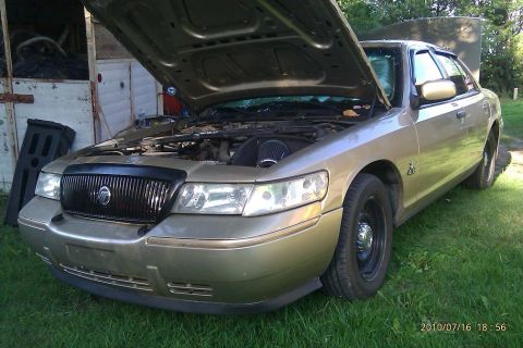 2000 Mercury Grand Marquis - A gold Mercury Grand Marquis is parked outside with its hood up, revealing the engine bay and an aftermarket air filter.