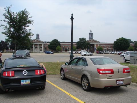 1992 Ford Taurus - A black Ford Mustang and a tan Lincoln MKZ are parked in a lot, with a large building in the background.