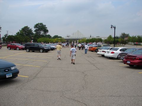 1992 Ford Taurus - A gathering of vehicles and people in a parking lot outside a large building.