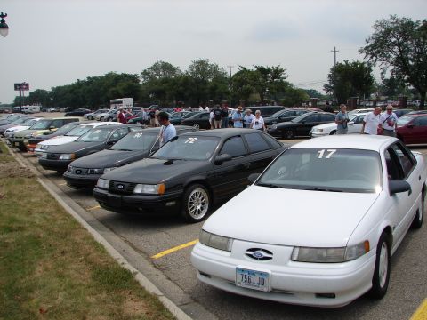 1992 Ford Taurus - A group of Ford Tauruses are parked in a lot, with some people milling around in the background.