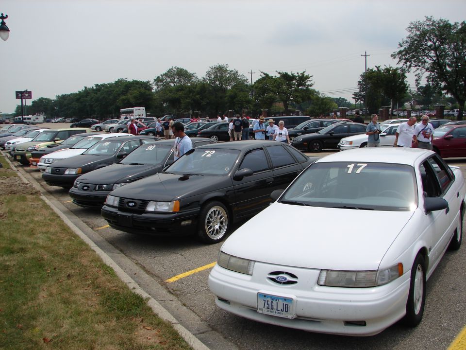 Several Ford Tauruses parked in a lot, one white one in foreground with number 17 on windshield