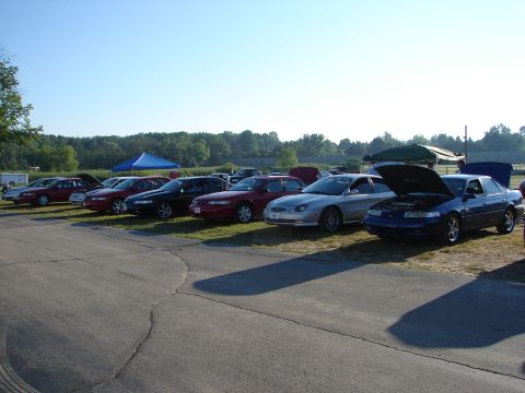 1992 Ford Taurus - Multiple sedans are parked on a grassy area under a clear sky, with trees in the distance.