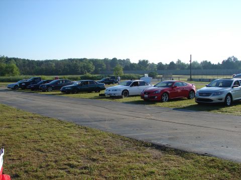 1992 Ford Taurus - Several cars are parked on a grassy area next to a paved surface under a clear sky.