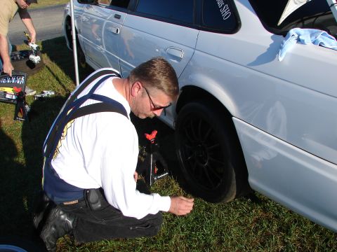1992 Ford Taurus - A man works on the rear tire of a white sedan with black wheels during an event.