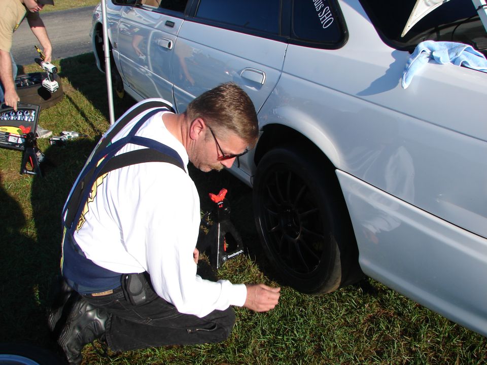 Side view of a white sedan with black wheels, a man works on the rear tire