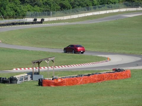 1992 Ford Taurus - A red sedan navigates a curve on a race track, with safety barriers in the foreground.