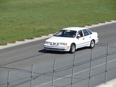1992 Ford Taurus - White 1992 Ford Taurus on a race track, driver wearing a helmet and race number 09 visible.