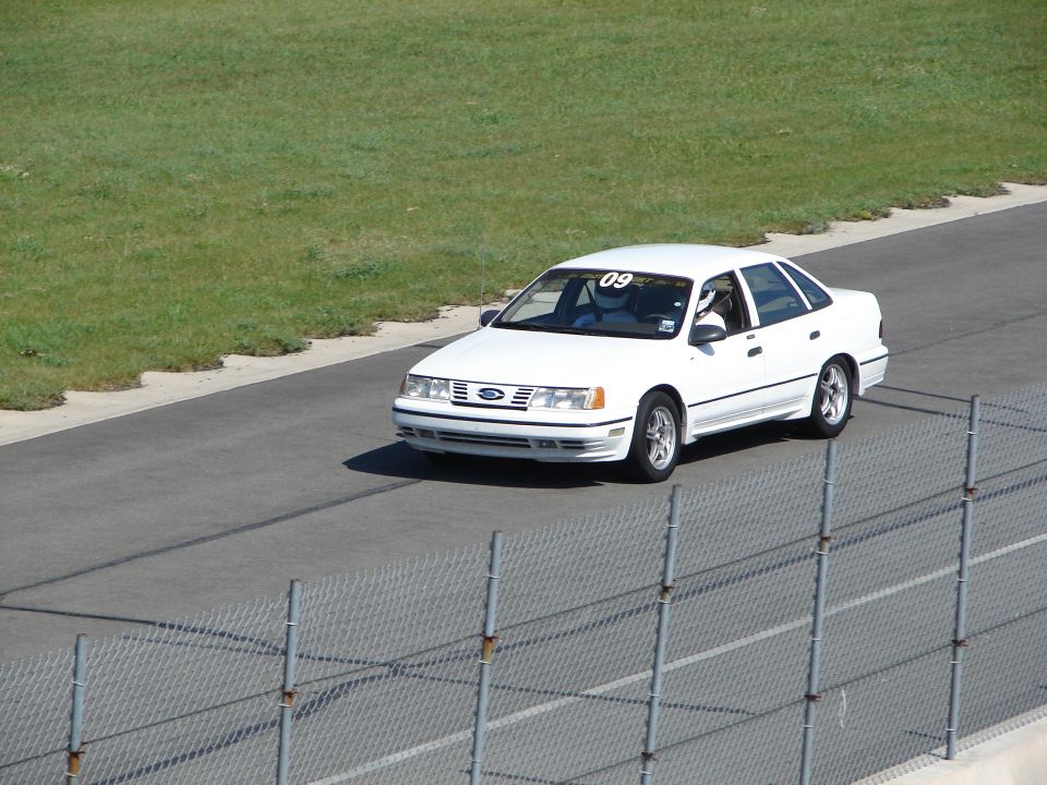 1992 Ford Taurus on a race track with driver wearing helmet and number 09 on windshield