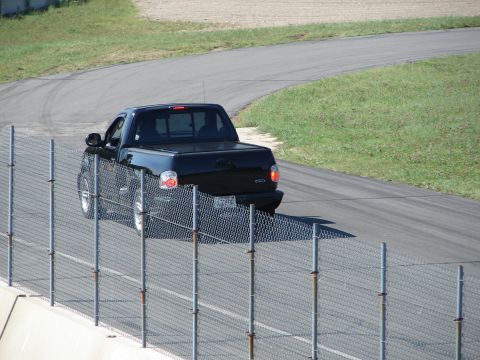 1992 Ford Taurus - Black 1999 Ford F-150 SVT Lightning pickup truck driving on a race track.