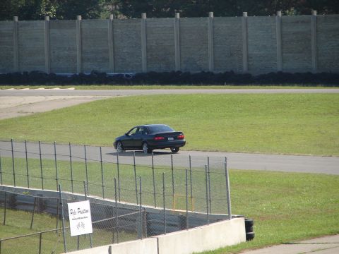 1992 Ford Taurus - A dark sedan is on the track, with a fence and grassy area in the foreground.
