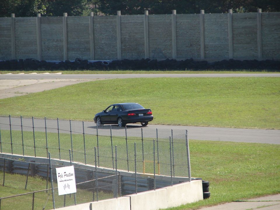 dark sedan driving on a race track, seen from behind