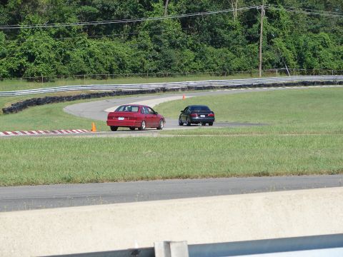 1992 Ford Taurus - Two sedans, one red and one black, navigate a turn on a race track.