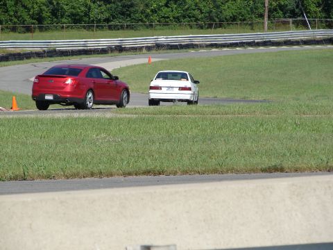 1992 Ford Taurus - Two sedans race on a track, with the red car in the foreground and the white car ahead.