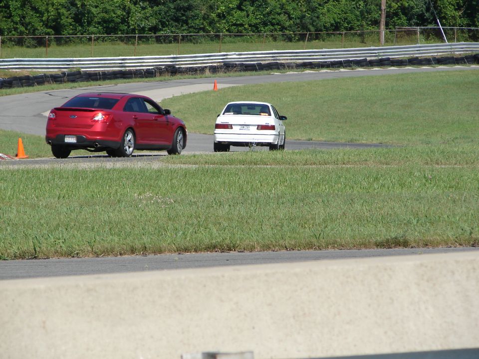 Red sedan on a race track with a white car ahead