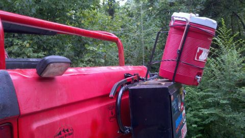 1979 Ford Bronco - A red vehicle is parked outdoors with a large red water cooler attached to the rear.