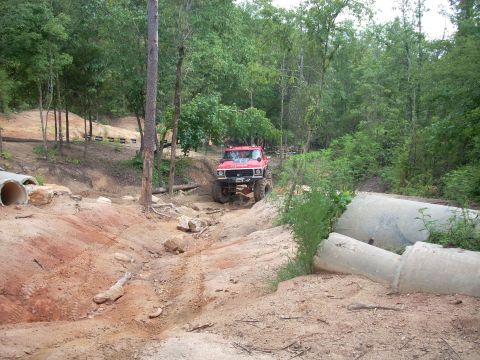 1979 Ford Bronco - A red off-road SUV navigates a challenging dirt trail with concrete pipes lining the path.