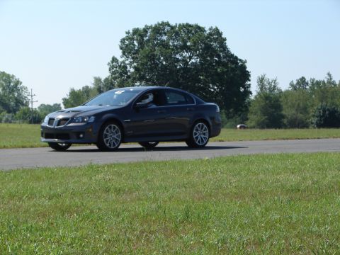 1992 Ford Taurus - A dark gray sedan with a driver wearing a helmet navigates a turn on a race track.