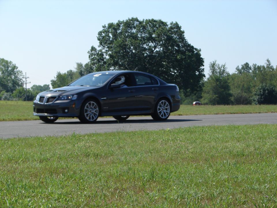 Dark gray sedan on race track, driver wearing helmet