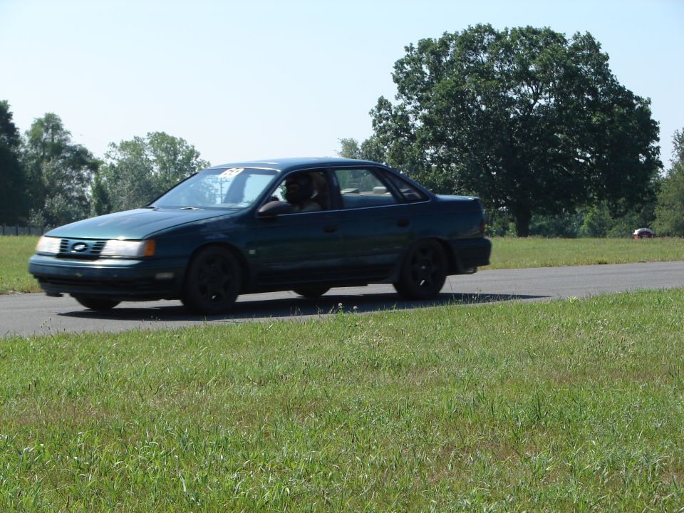 1992 Ford Taurus driving on a road with trees and grass in the background
