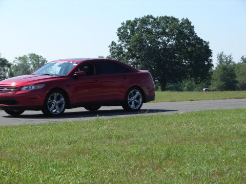 1992 Ford Taurus - A red sedan is captured in motion on a paved surface, with a distant vehicle also visible on the grounds.