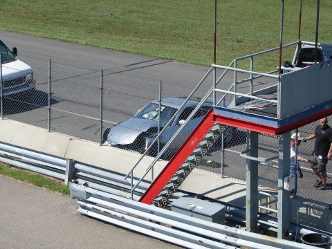1992 Ford Taurus - A silver sedan with its airbags deployed sits behind a fence on a race track, with a white van visible in the background.