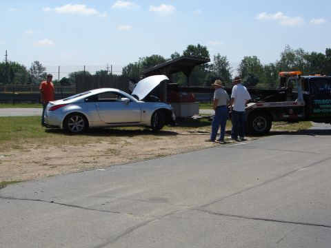 1992 Ford Taurus - A silver sports car with its hood open is attended to by two men, with a tow truck nearby.