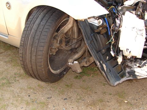 1992 Ford Taurus - The front wheel assembly of a car shows significant damage, with exposed wiring and broken suspension components.