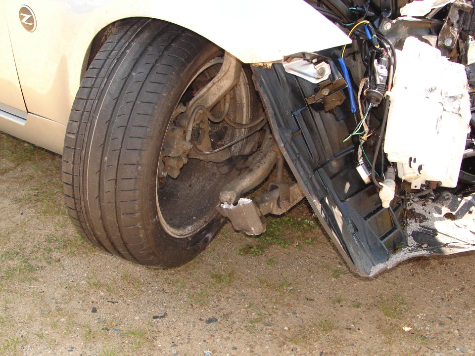 car's front wheel and suspension are damaged, with parts of the bumper missing
