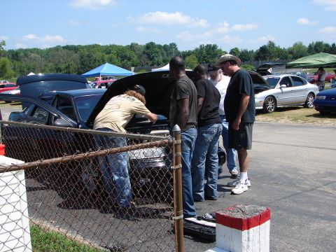 1992 Ford Taurus - Several people examine the engine of a black sedan at an outdoor event.