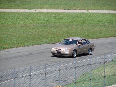 1992 Ford Taurus - A tan 1992 Ford Taurus is seen on a racetrack, displaying the number 76 on its windshield.