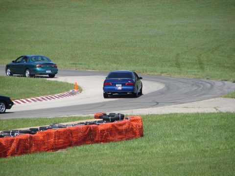 1992 Ford Taurus - A blue sedan navigates a curve on a race track, with another car visible in the background.
