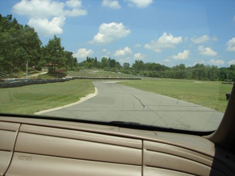 1992 Ford Taurus - View from inside a vehicle looking out at a race track on a sunny day, with a "SUPERMOTORS" logo visible on the dashboard.