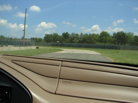 1992 Ford Taurus - View from inside a vehicle looking out at a racetrack with trees and a fence in the background.