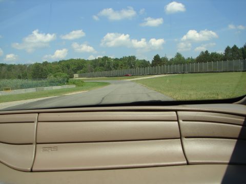 1992 Ford Taurus - View from inside a vehicle looking out at a race track on a sunny day with a distant red car.