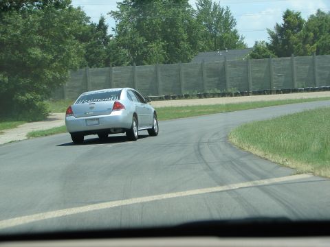 1992 Ford Taurus - A silver sedan with a 'CAUTION!!!' sticker on its rear window drives on a paved track.