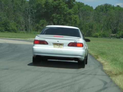 1992 Ford Taurus - Rear view of a white 1992 Ford Taurus on a road, with trees and a picnic area visible.