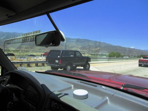 1986 Ford Bronco - Black SUV on highway with mountains in the distance.