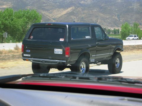 1986 Ford Bronco - This lifted Ford Bronco is seen on the road, with a white SUV in the background.