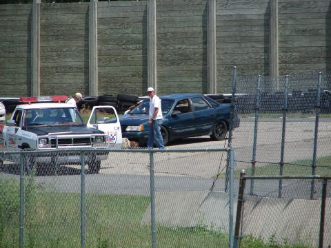 1992 Ford Taurus - A dark blue sedan with a spoiler is parked next to a utility truck.
