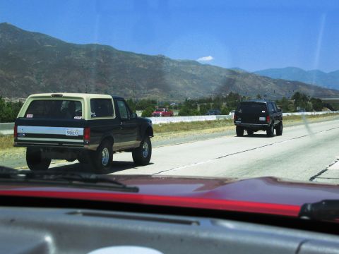 1986 Ford Bronco - A black and tan Ford Bronco drives down the highway, with another SUV in the distance.