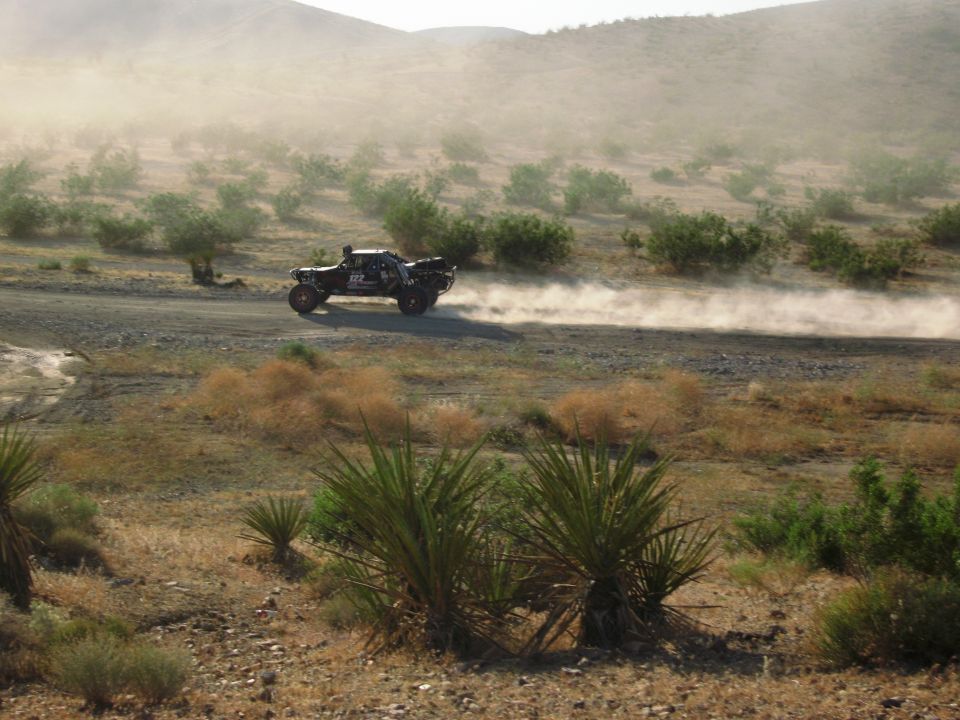 Off-road truck kicking up dust on a dirt road in a desert landscape