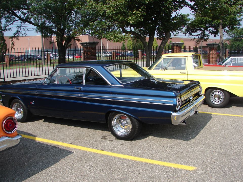Dark blue 1964 Ford Falcon coupe with chrome side trim and custom wheels, parked next to a yellow pickup truck
