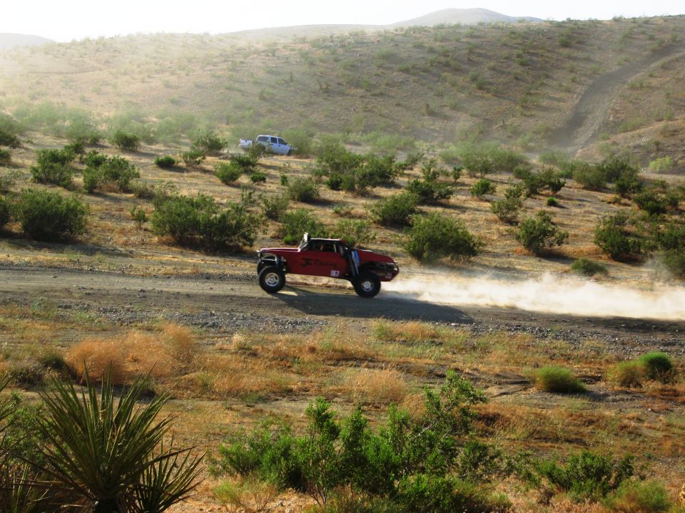 Red off-road truck kicking up dust on a dirt road in a desert landscape