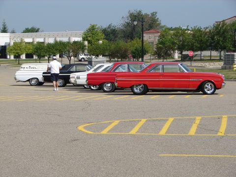 1992 Ford Taurus - A line of classic cars, including a red coupe and a white panel van, are parked in a lot.