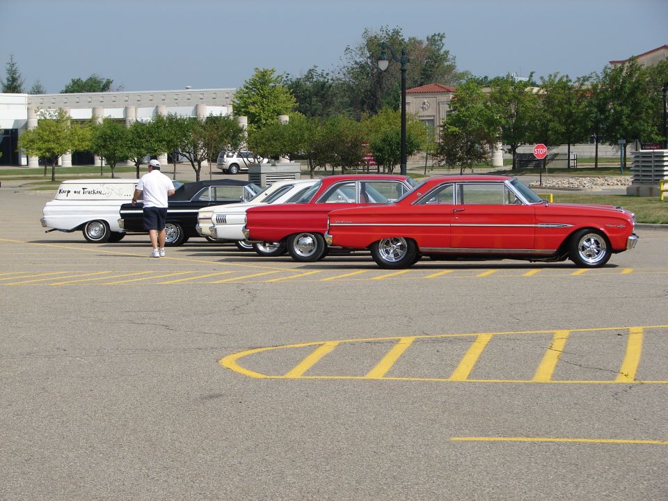 Red 1960s coupe parked in a lot with other classic cars